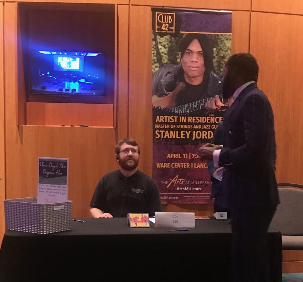 A man in a suit talking to a man behind a desk.