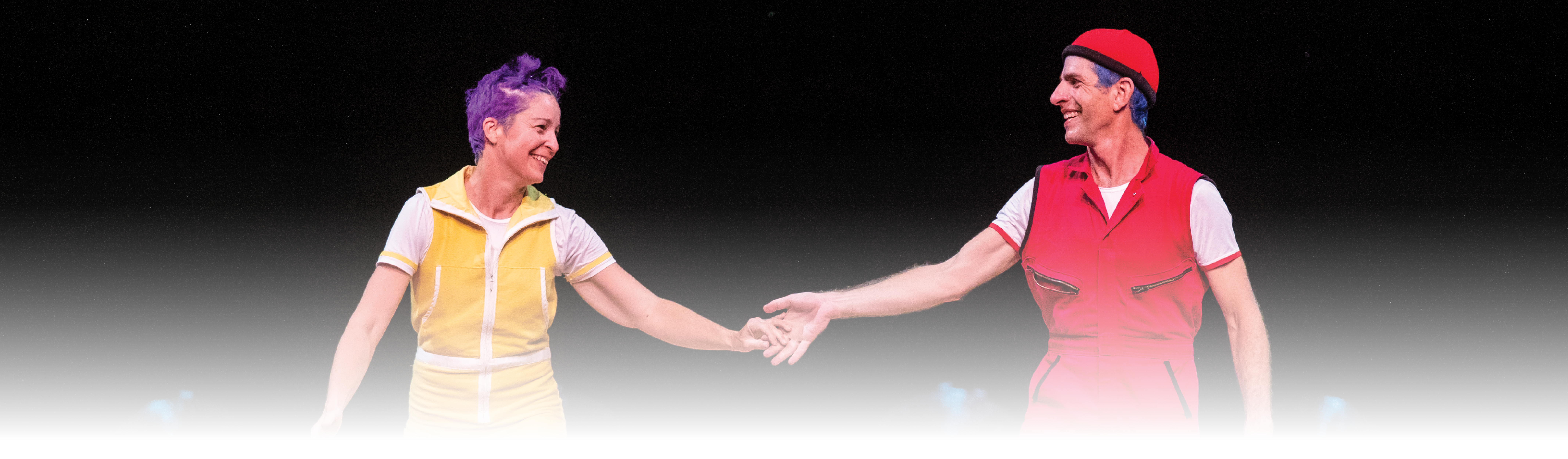A performer in yellow holds hands with a performer in red
